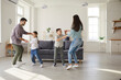 © Studio Romantic - Happy cheerful family playing and having fun at home. Joyful excited mom, dad and children dancing and enjoying leisure time together in modern white living room of new cozy house or studio apartment