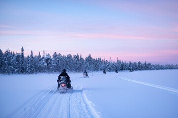 Snowmobiling on the frozen lake at sunset at Torassieppi, Lapland, Finland