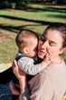 © DANIELMANUEL - Young woman playing with her baby in a public park on a sunny day