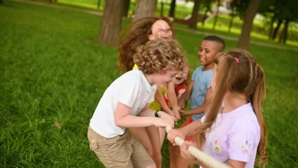 a group of children compete in a tug of war in the open air against the background of grass and park