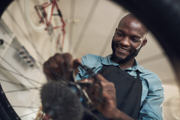 Aufkleber - This bike really needed a new part. Low angle shot of a handsome young man standing alone in his shop and repairing a bicycle wheel.