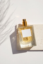 Transparent Bottle Of Perfume With White Label On Stone Plate On A White Background. Fragrance Presentation With Daylight. Trending Concept In Natural Materials With Plant Shadows. Women's And Men's
