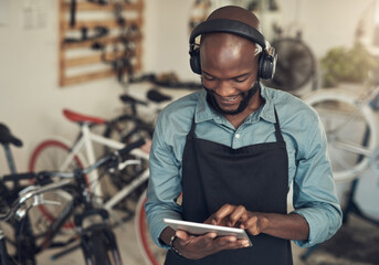 Aufkleber - We need good music in this store. Shot of a handsome young man standing alone in his bicycle shop and using a digital tablet while wearing headphones.