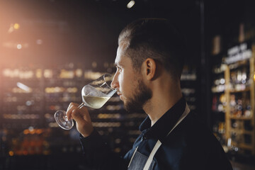 Sommelier man holds glass with white wine in restaurant, tests aroma and color