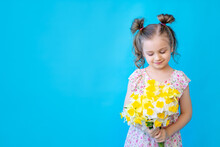 A Little Child Girl On A Blue Isolated Studio Background With Yellow Spring Flowers Daffodils. Space For Copying Text. Cute Kid