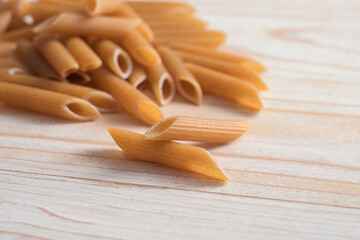 Wholemeal penne Rigate, healthy pasta alternative from whole grain durum wheat on a light wooden table, copy space, selected focus