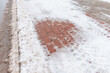 Melting snow on a pavement made of red concrete tiles in winter.