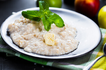 on a plate sweet oatmeal with butter, cherry tomatoes, cutlery on a black isolated background, top