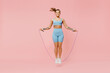 Full body young sporty athletic fitness trainer instructor woman wear blue tracksuit spend time in home gym using skipping rope isolated on pastel plain light pink background. Workout sport concept.