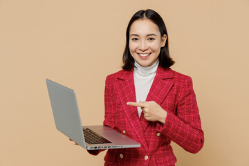 Wall Mural - Smiling happy fun copywriter student woman of Asian ethnicity 20s wear red jacket hold use work point on laptop pc computer isolated on plain pastel beige background studio. People lifestyle concept.