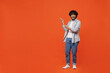 © ViDi Studio - Full size body length fun young bearded Indian man 20s years old wears blue shirt pointing index fingers aside on workspace area copy space mock up isolated on plain orange background studio portrait.