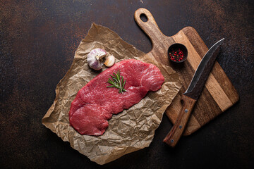 Canvas Print - Beef lean raw fillet steak on baking paper with rosemary, garlic and spices on dark brown rustic concrete background with knife from above flat lay, diet beef meat steak ready to be cooked, copy space