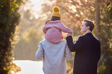 Wall Mural - Rear View Of Family With Two Dads On Walk In Winter Countryside Carrying Daughter On Shoulders