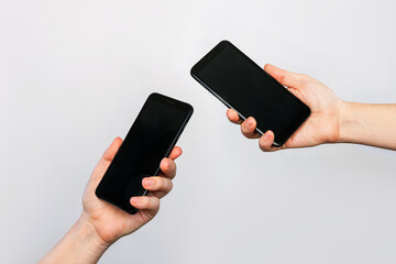 two hands of two women holding mobile phones with blank black screens, empty copy space for design i