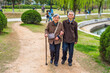 Senior Man and Woman Walking Outside. A  senior couple, 80 years old, helping each other, arm in arm,  is walking on a park, woman holding a walking stick..