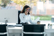 © nenetus - Smiling woman talking with her smartphone while working with computer in the modern startup office.