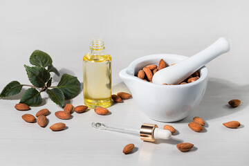 Almond oil in a bottle, pipette, bowl with almond kernels on a light background, natural organic cosmetic oil