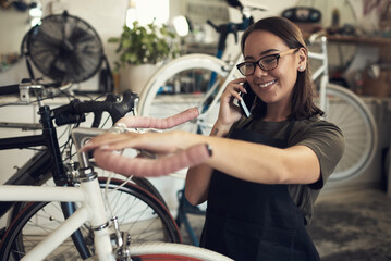 Aufkleber - Ive got your bike ready for pickup. Shot of an attractive young woman standing alone in her shop and repairing a bicycle wheel while using her cellphone.