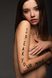 © LIGHTFIELD STUDIOS - naked woman with speak your mind lettering on arm looking at camera isolated on dark grey