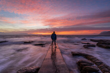 View Of A Person Standing At End Of The Pier Watching Pink Sunrise, Kalk Bay, Cape Town, South Africa.