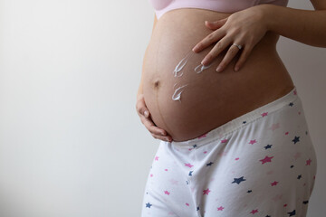 Wall Mural - A closeup shot of a pregnant woman rubbing cream on her belly