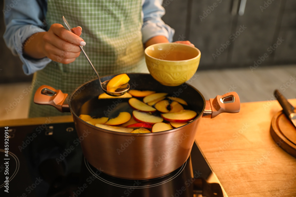Woman pouring compote to cup in kitchen, closeup