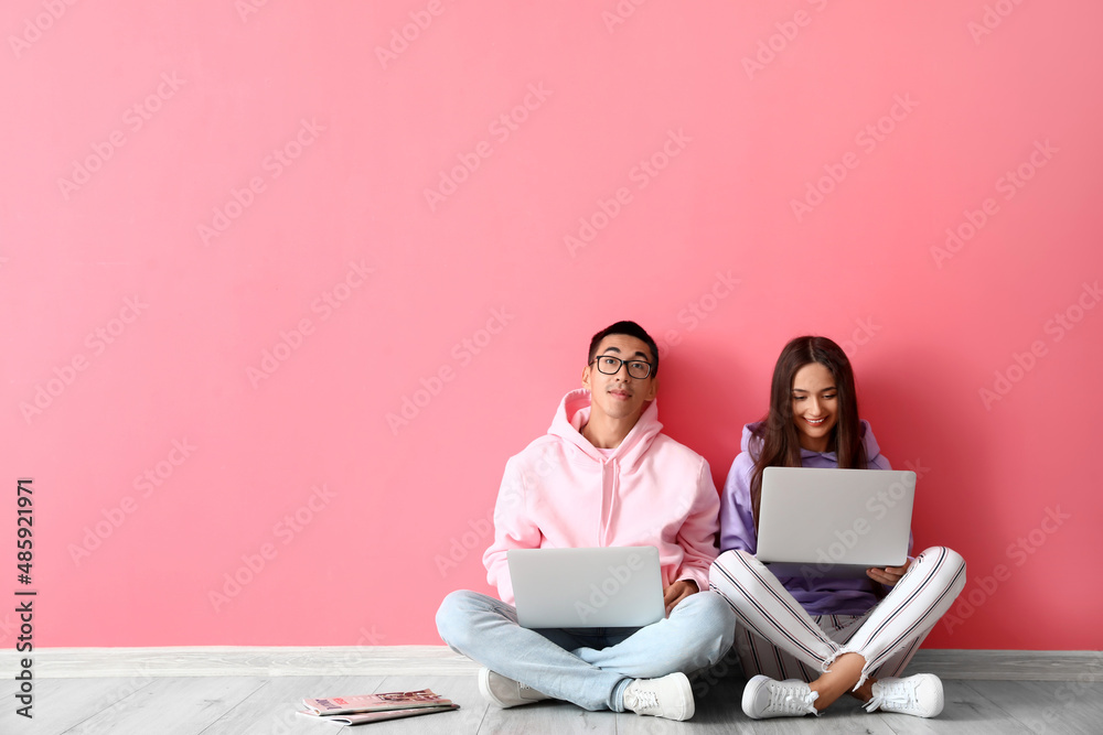 Young couple using laptops near pink wall