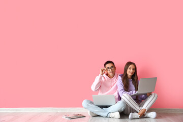 Wall Mural - Young couple with laptops sitting near pink wall