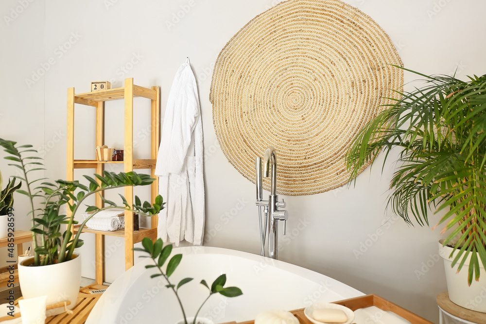 Interior of stylish bathroom with hanging wicker carpet on light wall