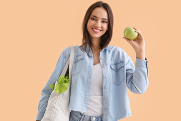 Wall Mural - Young woman with eco bag and apple on beige background