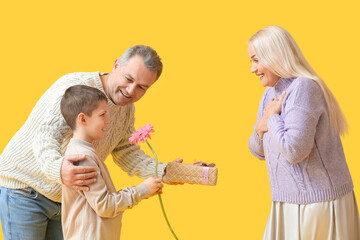 Wall Mural - Senior man with little grandson greeting his wife on yellow background