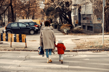 A young mother holding hands with her preschooler and crossing the street.