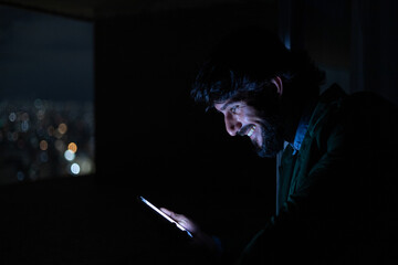 Side view of young man using a smartphone at night time with city view landscape in the background. High quality photo