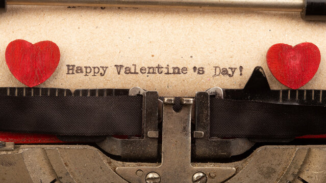 Happy Valentine`s day - phrase on typewriter. Valentines Day greetings concept. Little red wooden heart close up. Valentines greeting card.