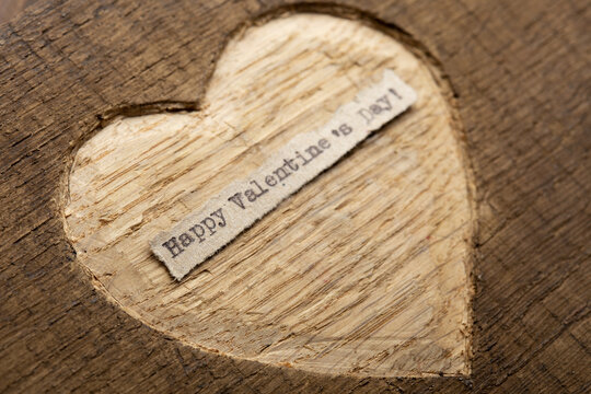 Happy Valentine's day - tiny typed text note close up. Valentines Day greetings concept. Carved heart shape on wood as background for Valentines greeting card.