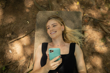 Young woman using a smartphone at day time lying down on a bench at a park. High quality photo