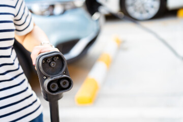 Unrecognizable Asian woman holding aa DC - CCS type 2 EV charging connector at EV charging station.