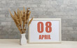 April 8. 8th day of month, calendar date.  White vase with ikebana and photo frame with numbers on desktop, opposite brick wall. Concept of day of year, time planner, spring month