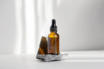 Wall Mural - Serum in glass bottle with dropper lid on stand made of natural granite stone. Essential oil for care of women's skin on white background, in rays of sunlight. Space for copying, glare on object