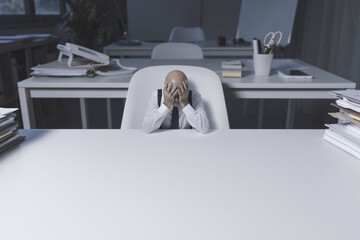 Wall Mural - Tiny businessman sitting at desk and feeling desperate