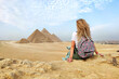 Egypt. Cairo Giza. young blonde tourist girl with a backpack is sitting on the sand looking at General view of pyramids from the Giza Plateau. enjoy the beautiful view and relax. concept of tourism.