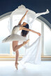 Young motivated ballerina dressed in white tutu costume practice ballet moves at ballet studio in front of big round shaped window background in natural ambient daylight atmosphere