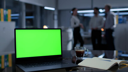 Laptop with green screen on desk and business people talking on blurred background