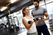 © NDABCREATIVITY - Fit happy woman with her personal fitness trainer in the gym exercising with dumbbells