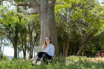 Young woman using a laptop at day time with a green park in the background. High quality photo