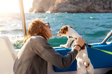Back View Young Adult Caucasian Woman Enjoy Petting Cute Adorable Little Jack Russel Dog Sailing Family Luxury Yacht Boat Against Blue Water Bright Sunny Summer Day. Travel Sea Tourism With Pets