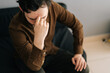 © dikushin - Close-up of stressed young man sitting alone feeling sad worry regret or fear, holding hand on forehead, depressed and desperate home. Suffering emotional pain and unhappy, mental health.