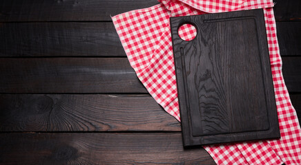 Wall Mural - wooden cutting board and folded red and white cotton kitchen napkin on a wooden brown background, top view