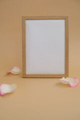 Mockup Wooden frame with Empty white paper blank and delicate pink rose petals on beige background. Minimal trendy composition. Romantic pastel pink rose flowers. Neutral earth tones. Copy space