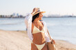 © Syda Productions - people, summer and leisure concept - portrait of young woman in bikini swimsuit, white shirt and straw hat with bag on beach